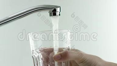 在视频中，一个水龙头，水运行，手带来一个玻璃不倒翁到水龙头，玻璃完全充满了水